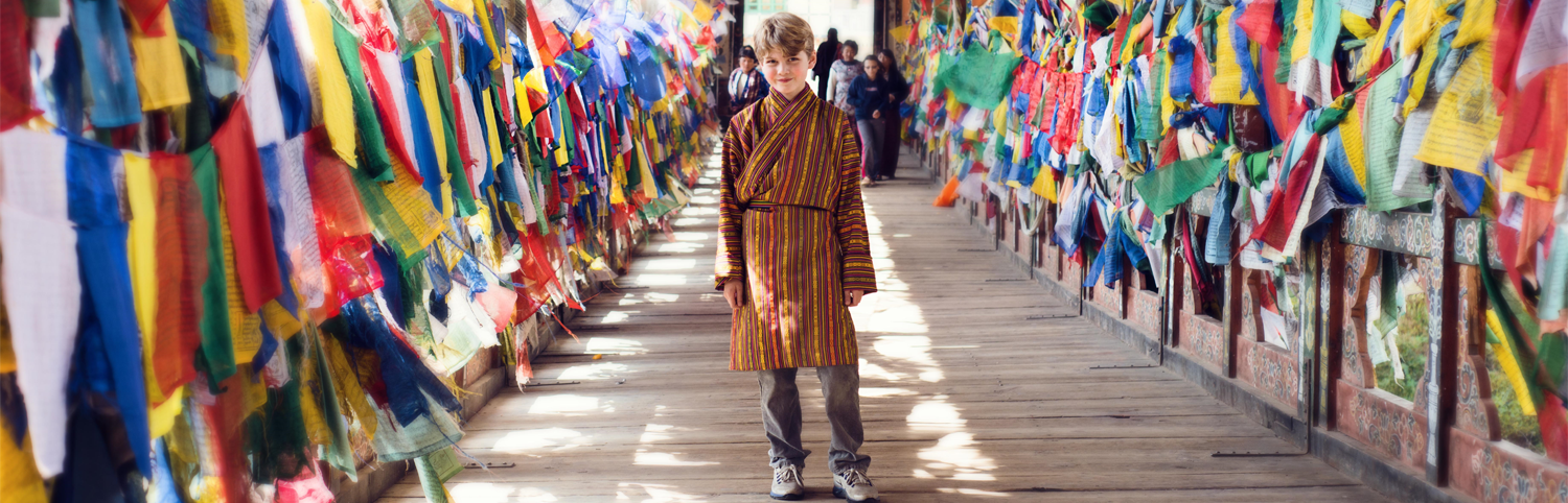 Young boy walking on a bridge in Bhutan lined with prayer flags