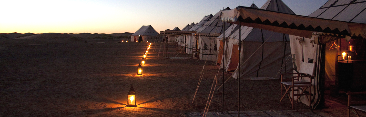 Evening view of a camp in the Sahara Desert with several tents. 